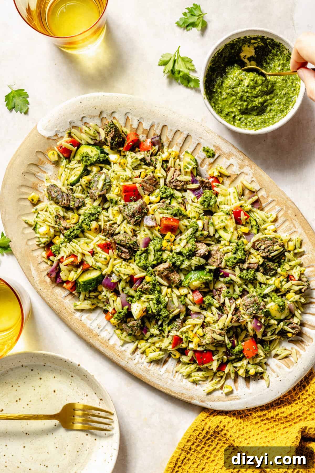 Grilled Steak and Chimichurri Pasta Salad on platter with extra sauce on side as well as plates and napkins.