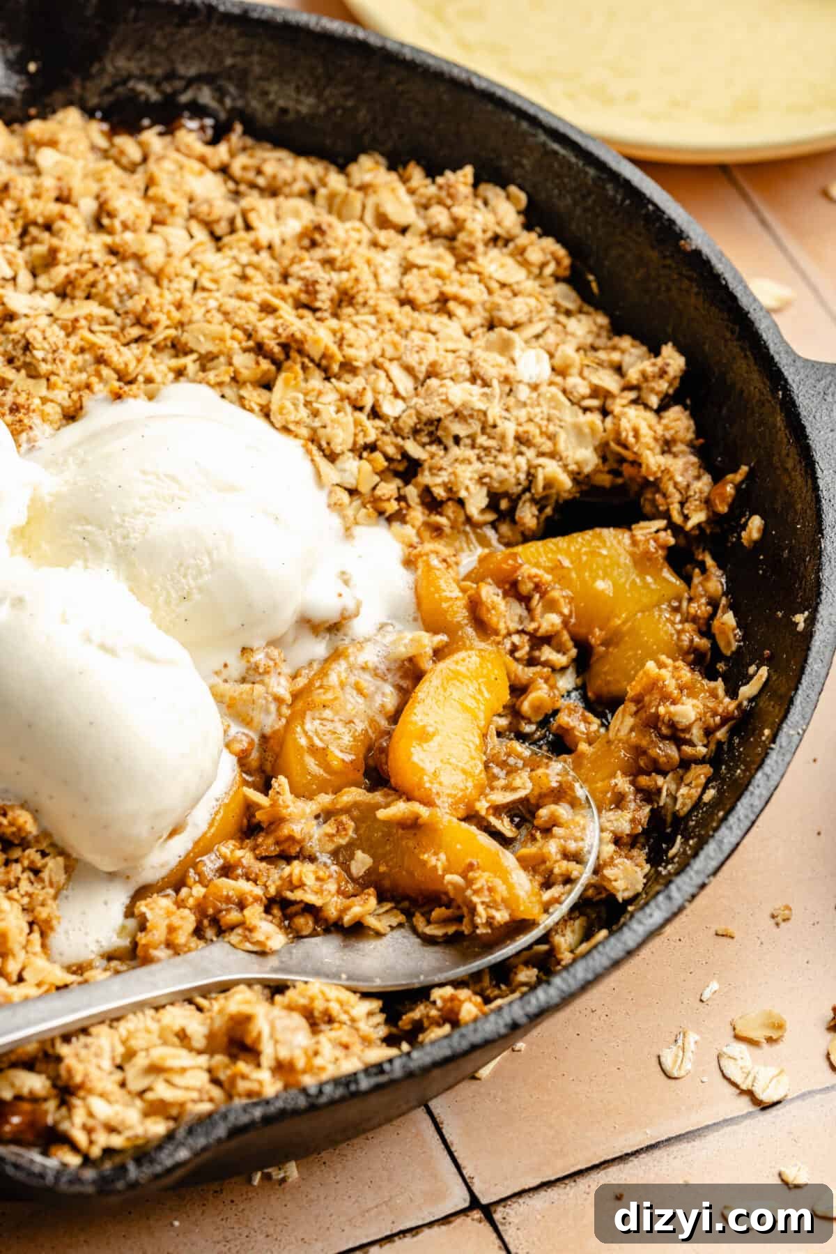 Close up of simple Skillet Peach Crumble in black cast iron skillet with three scoops of vanilla ice cream on top.