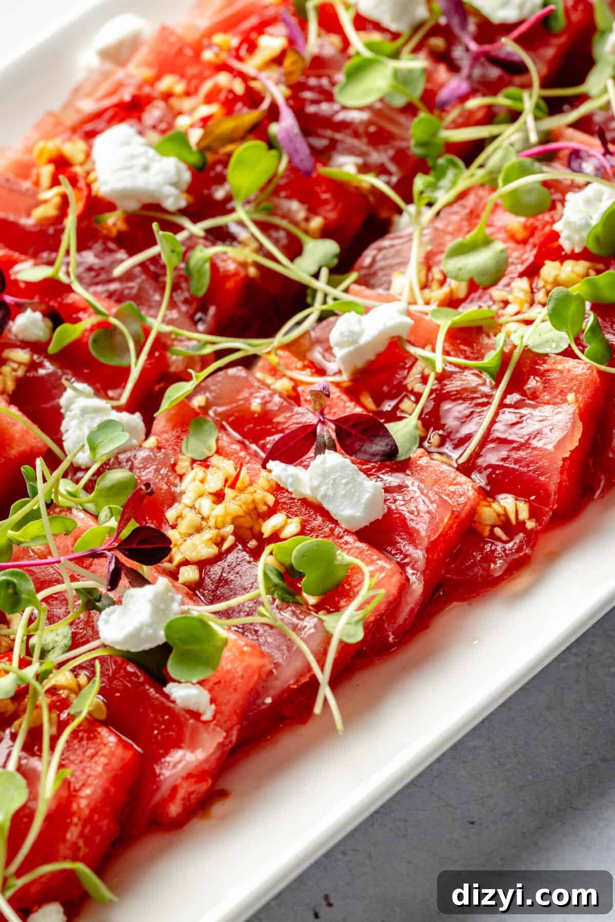 Watermelon and Tuna Sashimi Recipe 3 Close-up of layered watermelon and ahi tuna topped with microgreens, goat cheese, and a drizzle of sauce.
