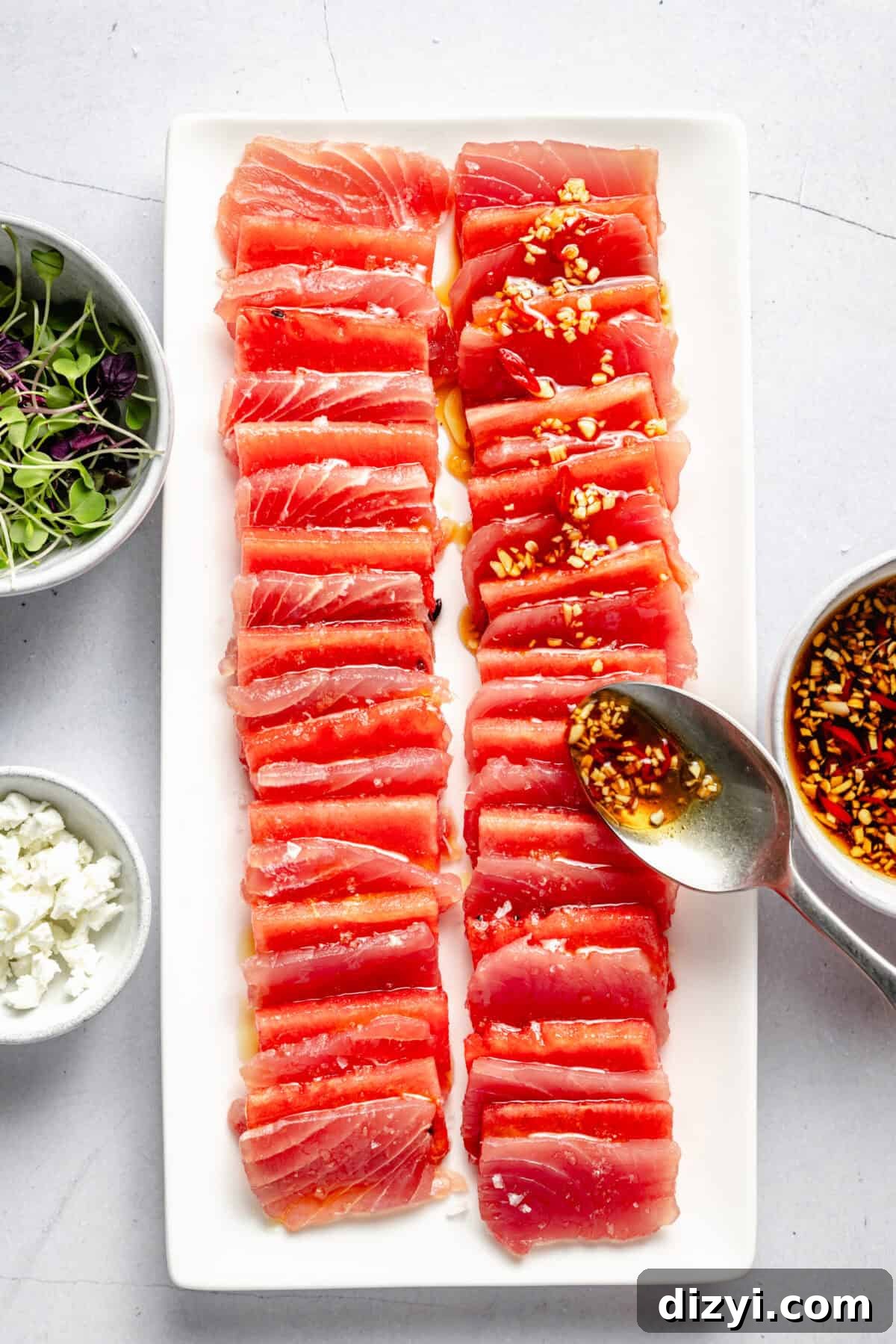 Watermelon and Tuna Sashimi Recipe 5 Platter showing domino-size pieces of watermelon and ahi tuna layered with small bowls of microgreens and crumbled goat cheese nearby.