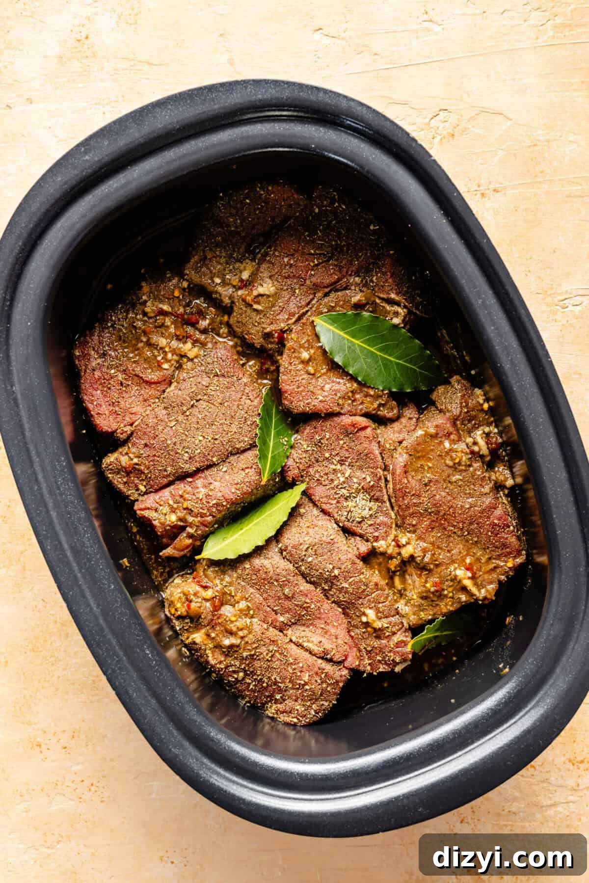 Beef, seasonings, and bay leaves in the bottom of a slow cooker.