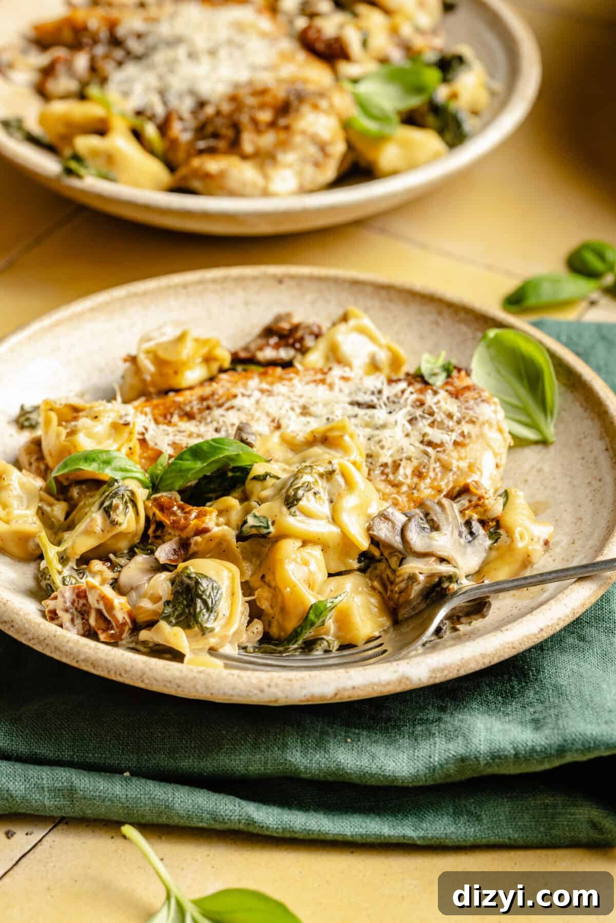 One-Pan Creamy Chicken and Tortellini Bake 4 Two tan plates of Creamy Spinach Chicken and Tortellini Bake, one sitting on top of a dark green napkin.