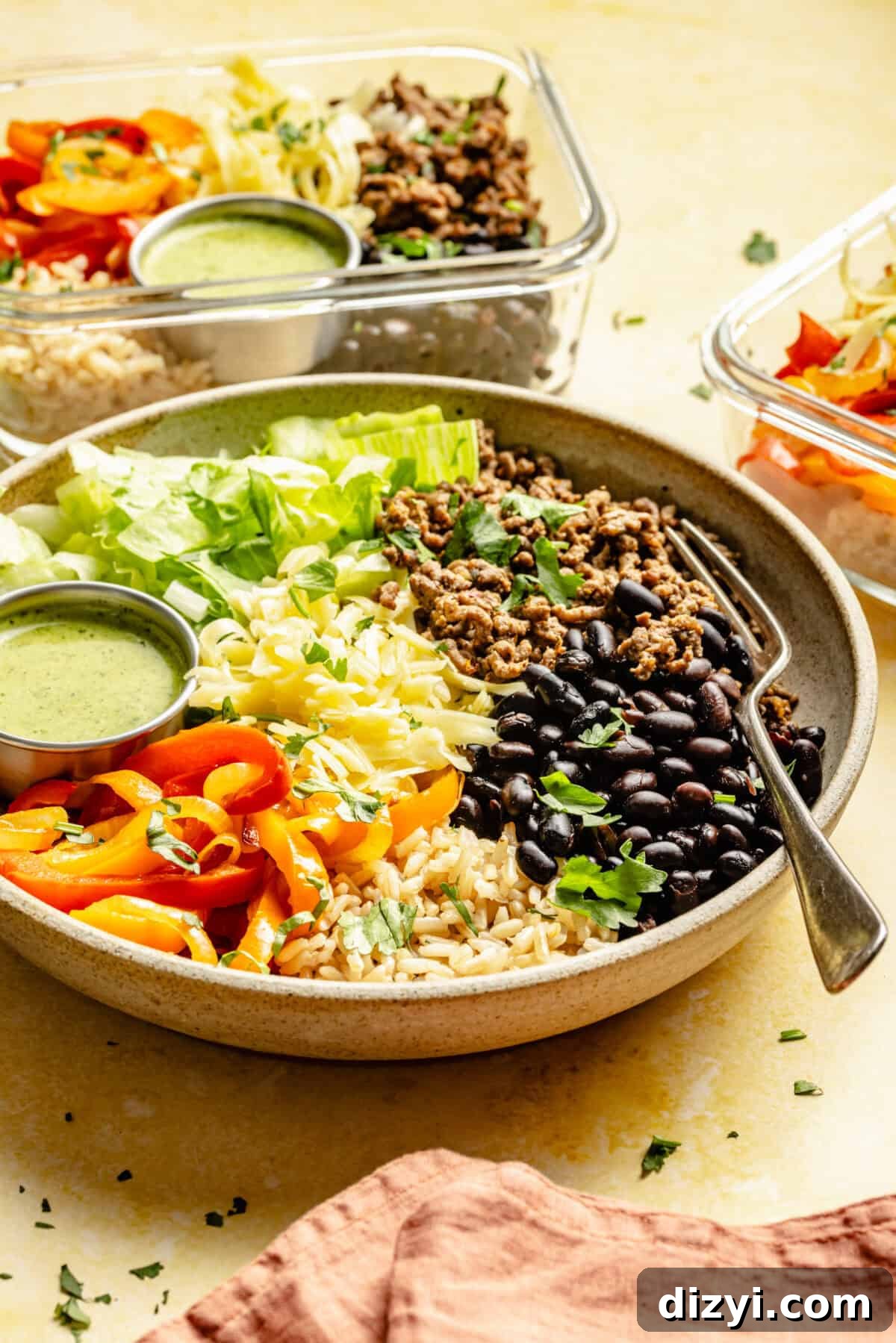 Meal-Prep Taco Bowls with Jalapeno Dressing 2 A finished taco bowl in a tan dish on a beige counter. Two glass meal prep containers are visible in the back. An amber colored napkin is also on the table.