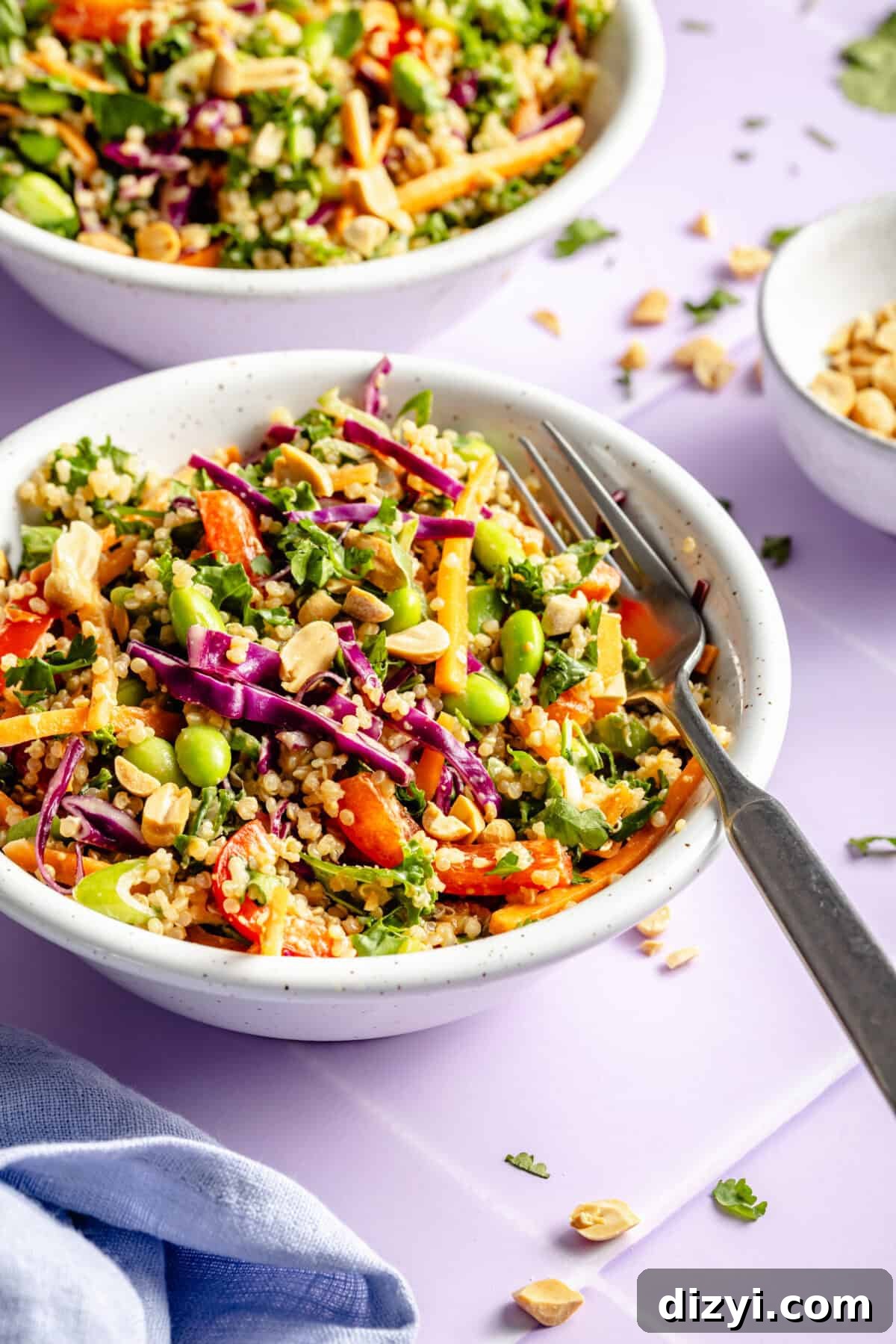 Crunchy Thai Quinoa Salad with Peanut Lime Dressing 3 A side view of a white bowl of Crunchy Thai Quinoa Salad with a silver fork. A couple of other bowls are barely visible in the background.