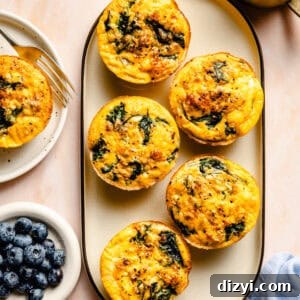 A top-down view of a platter of Sausage and Egg Mini Frittatas on a countertop. There's a dish of blueberries next to the platter.