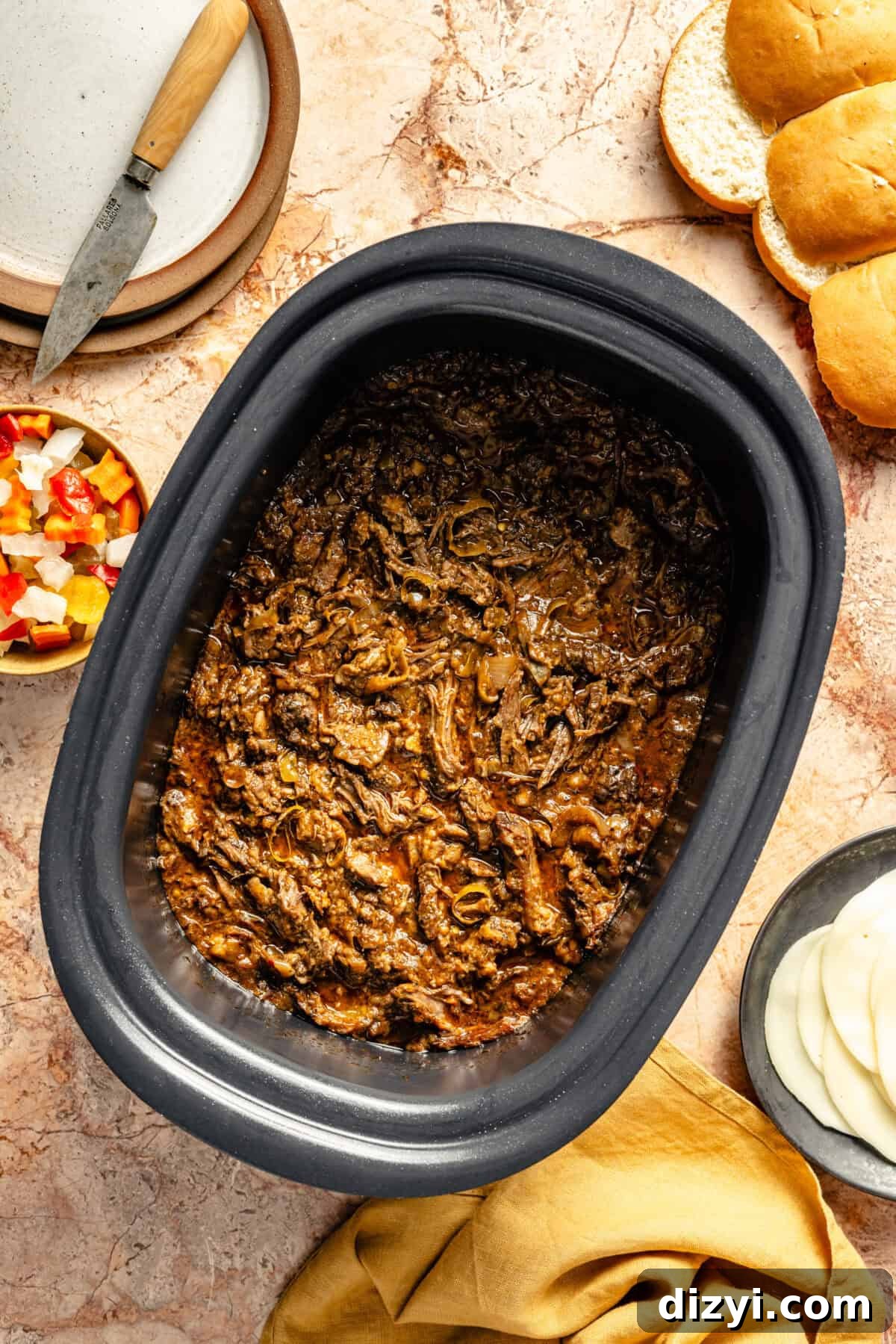 Slow Cooker Italian Shredded Beef Sliders Recipe 7 The shredded meat for the Slow Cooker Italian Shredded Beef Sliders in the slow cooker, with the other ingredients for the sliders in dishes surrounding it.