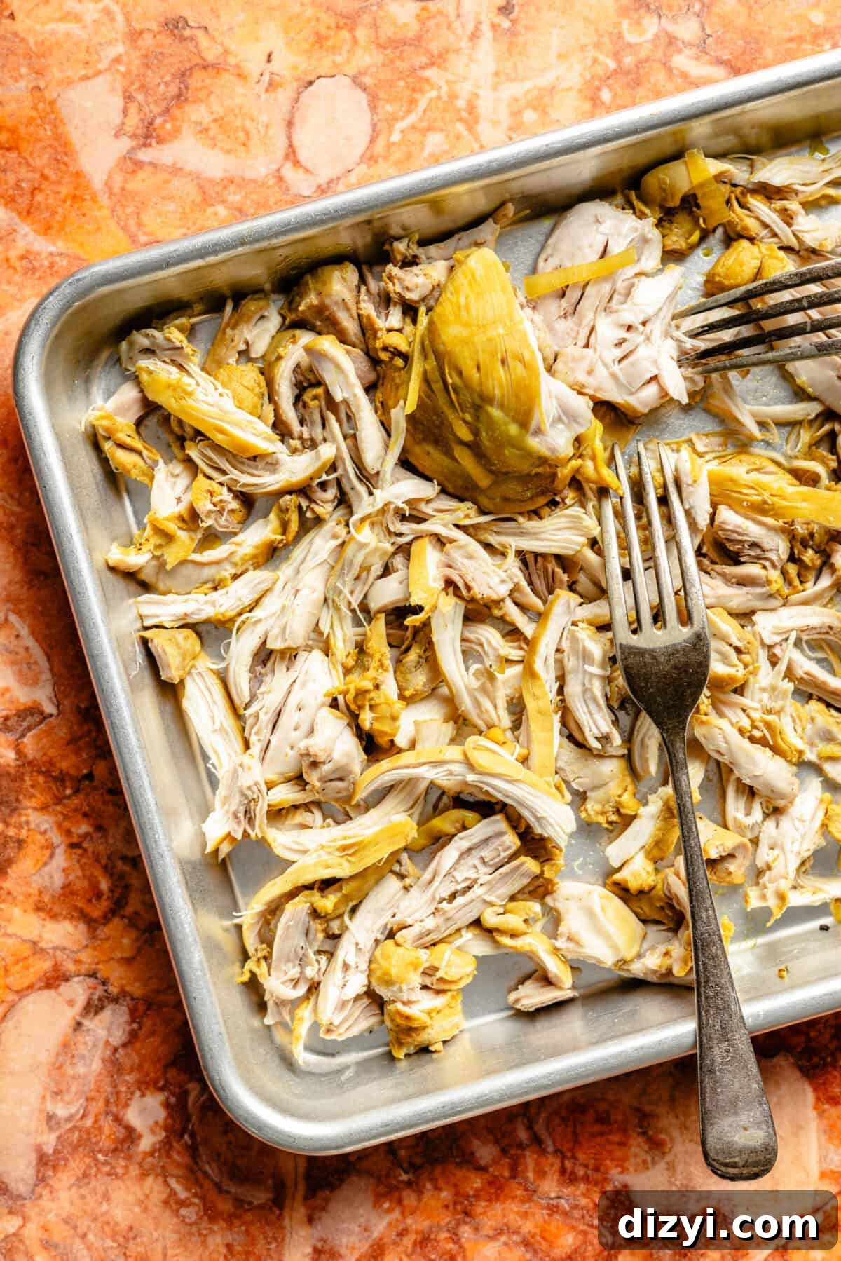 A sheet pan with two forks shredding chicken on top of an orange countertop.