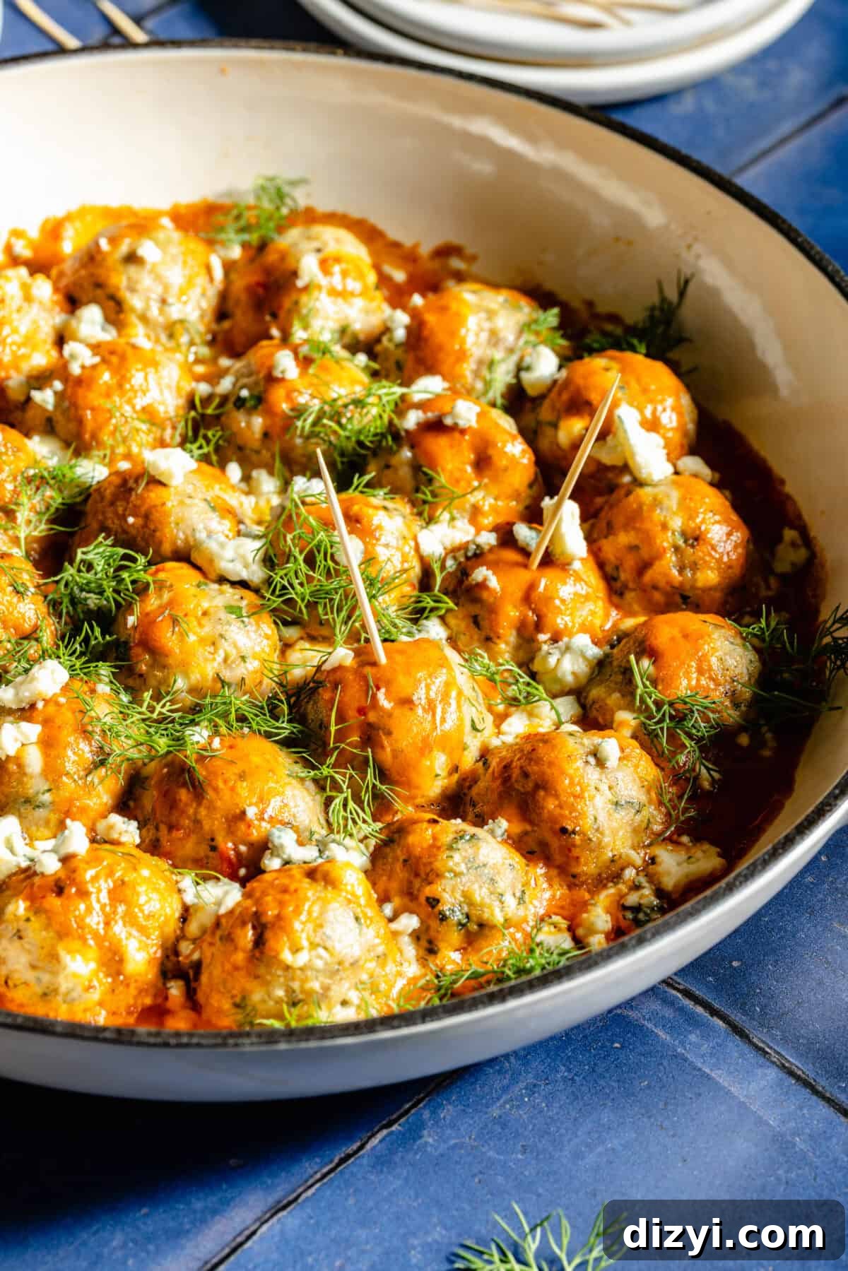 A close-up shot of the Buffalo Chicken Meatballs in a shallow gray dish on top of a blue tile countertop.