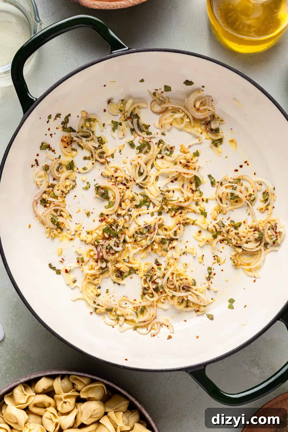 Shallot, garlic, sage, and red pepper flakes cooking on the stove to make Creamy Pumpkin Tortellini.