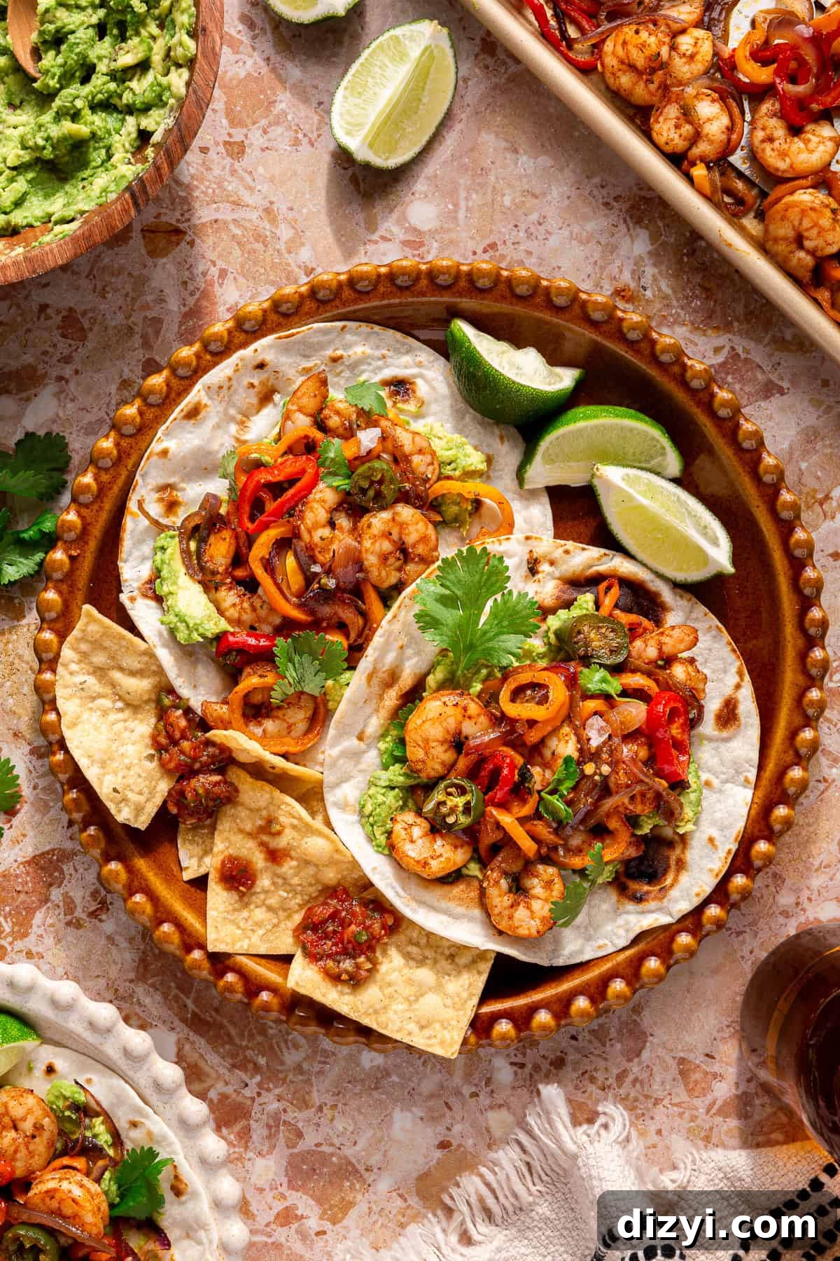 A finished bowl of Sheet Pan Shrimp Fajita Tacos, garnished with cilantro, lime wedges, and chips.