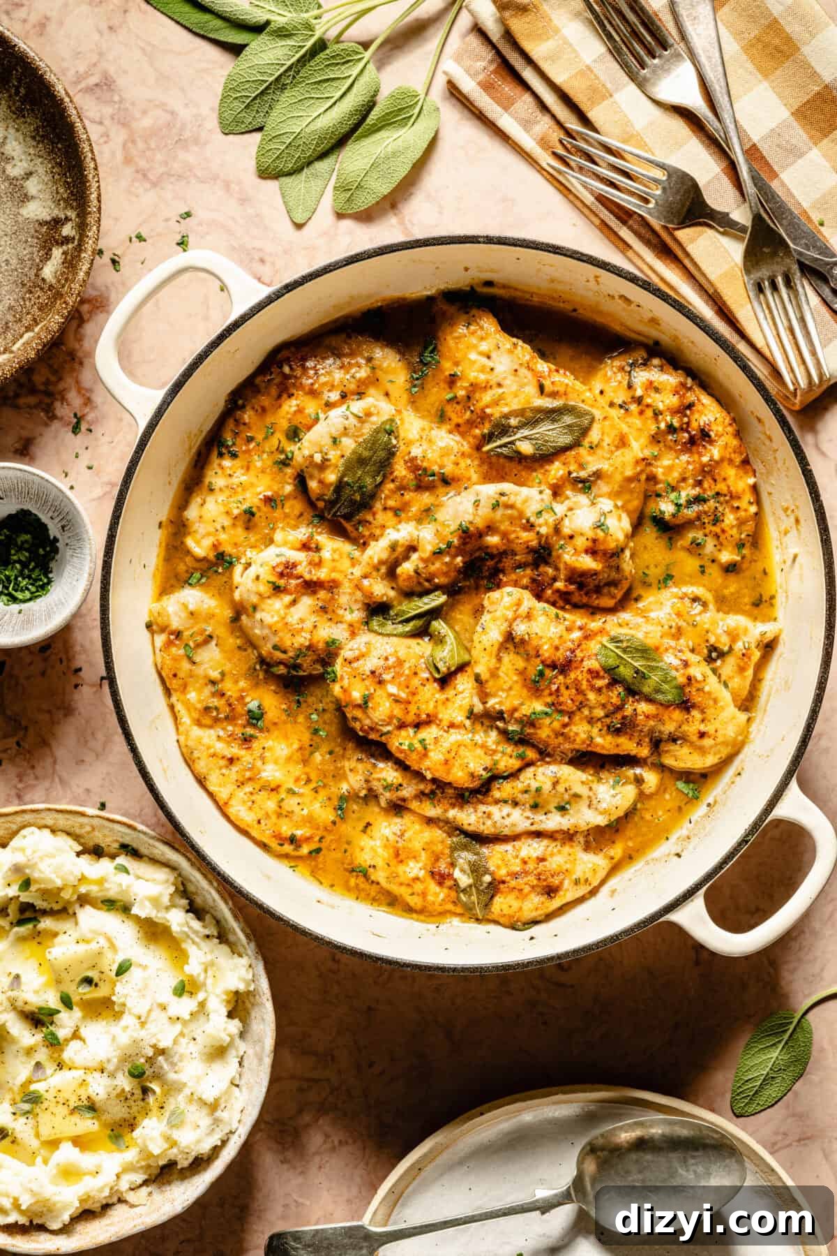 A top-down view of Chicken with Herby White Wine Gravy in a white skillet with a silver spoon, garnished with sage.