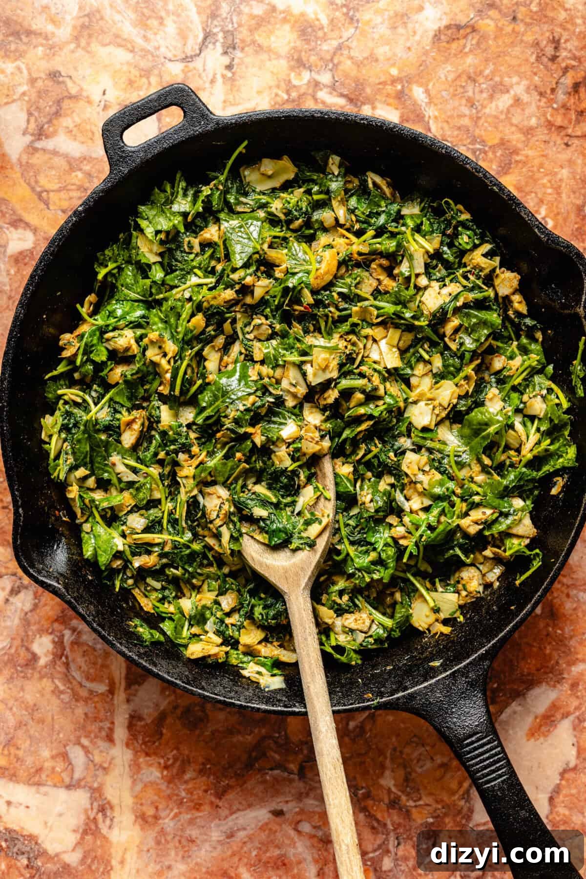 The spinach, kale, and artichokes sauteeing in a black cast iron skillet for the Skillet Spinach, Artichoke, and Kale Dip.