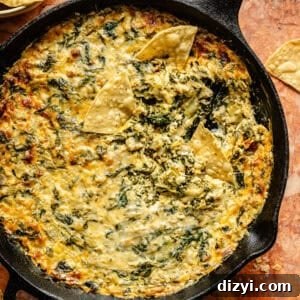 A top down view of Skillet Spinach, Artichoke, and Kale Dip with a chip dipping into it.