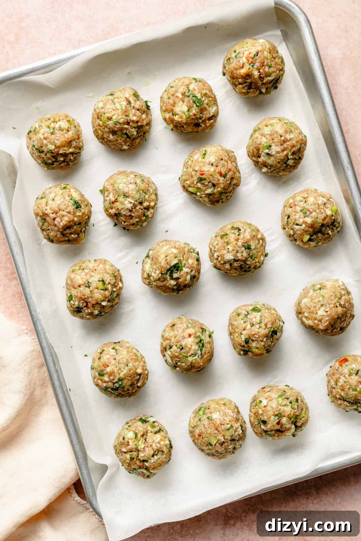 A tray of meatballs assembled for Ginger-Pork Meatball Pho and ready to go into the oven. The meatballs are on a silver baking tray with parchment paper.
