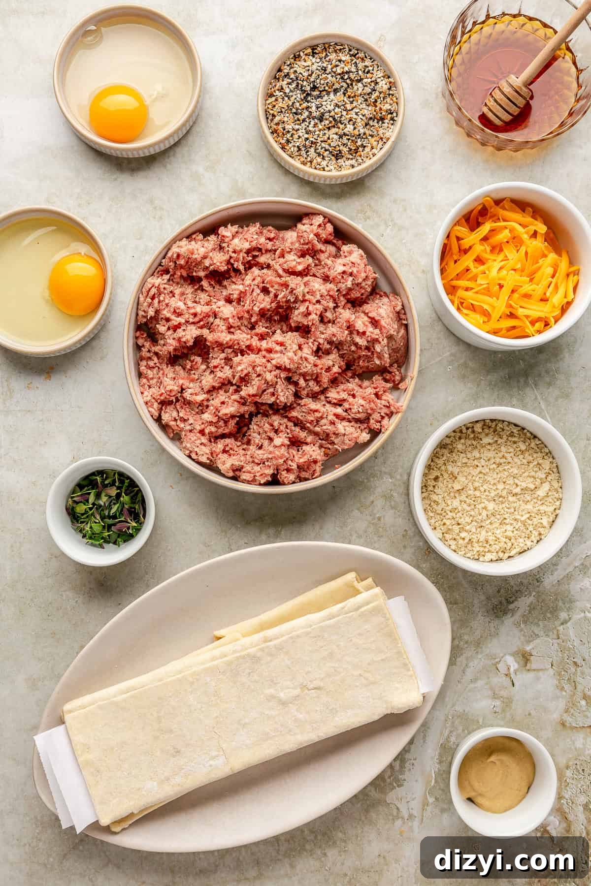 The ingredients needed for Sausage Rolls with Hot Honey and Thyme in various dishes and bowls spread on a gray countertop.