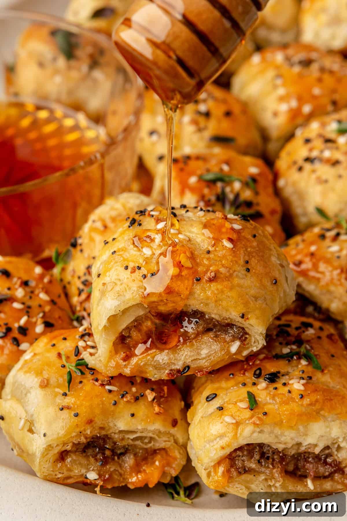 A super close-up shot of a Sausage Rolls with Hot Honey and Thyme with the hot honey being drizzled on it.