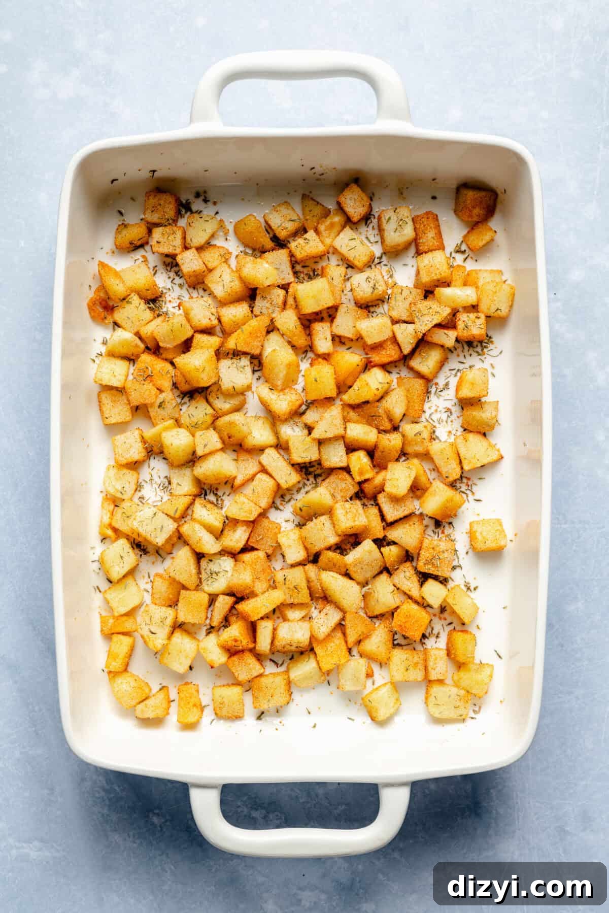 Classic Old Fashioned Breakfast Casserole Recipe 5 The potatoes for Old Fashioned Breakfast Casserole in the bottom of a white casserole dish on a white countertop.