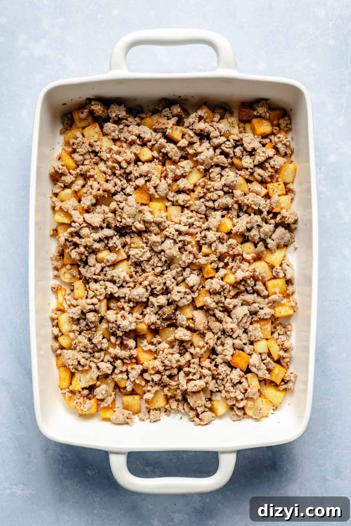 Classic Old Fashioned Breakfast Casserole Recipe 6 The browned meat and potatoes for Old Fashioned Breakfast Casserole in the bottom of a white casserole dish on a white countertop.