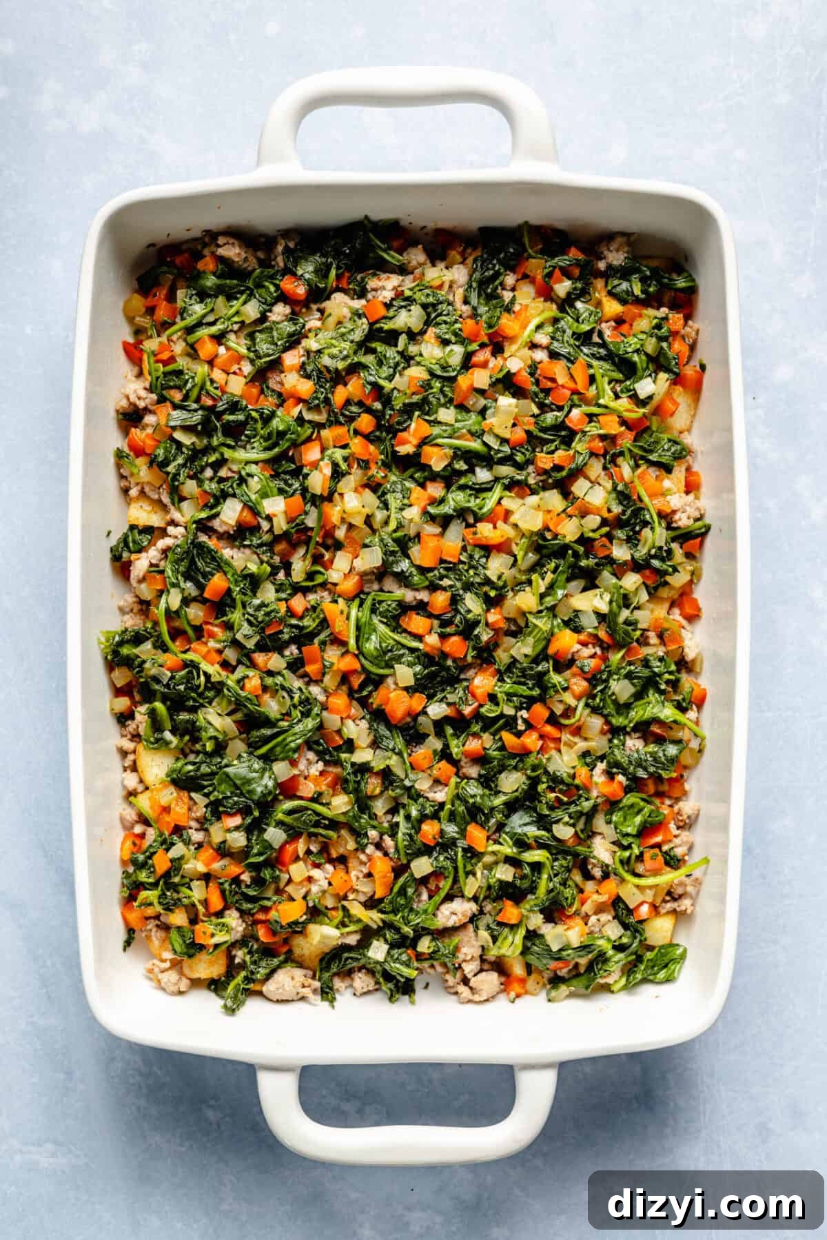 Classic Old Fashioned Breakfast Casserole Recipe 7 The browned meat, veggies, and potatoes for Old Fashioned Breakfast Casserole in a white casserole dish on a white countertop.