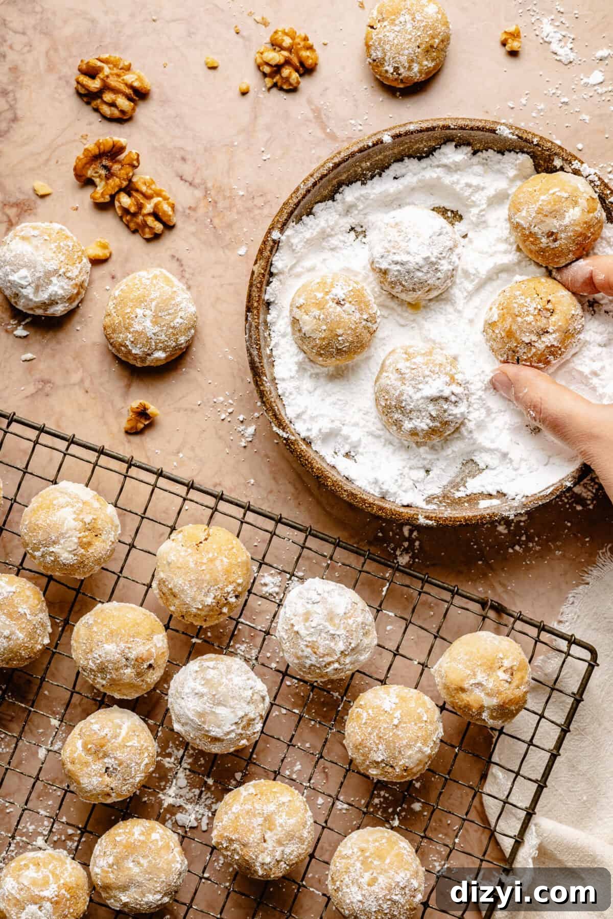 The baked GoGo's Russian Teacakes on a wire cooling rack, and a few getting rolled in powdered sugar on a tan countertop.