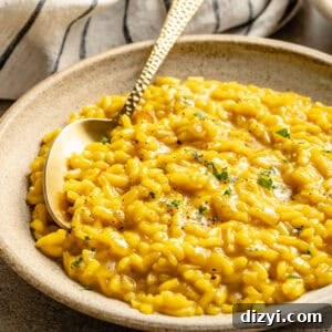 A side image of a finished bowl of Risotto Milanese on a tan countertop. A cream and black striped napkin is visible in the image as well.