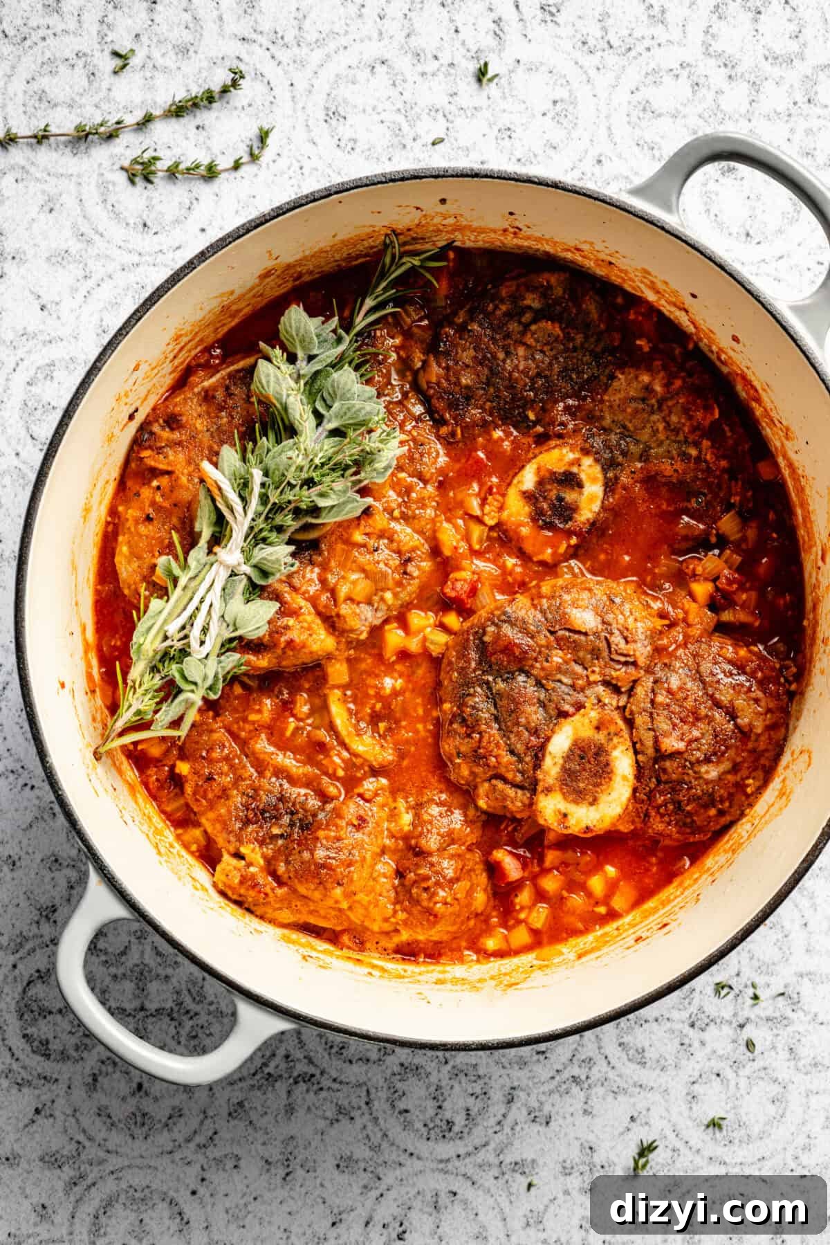 Osso Buco cooking in a stockpot with the bundle of herbs on a white and black countertop.
