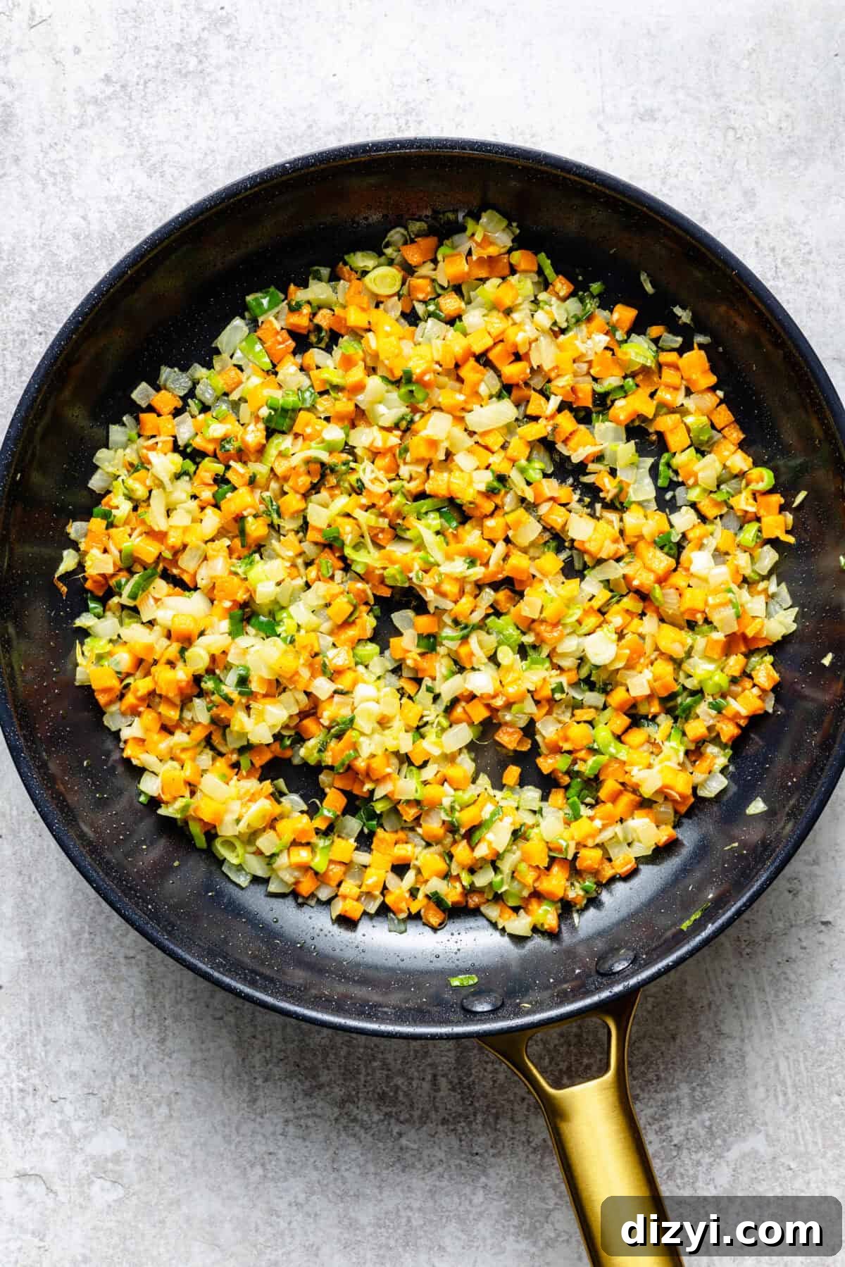 The veggies for Simple Chicken Fried Rice cooking in a black skillet with a gold handle.