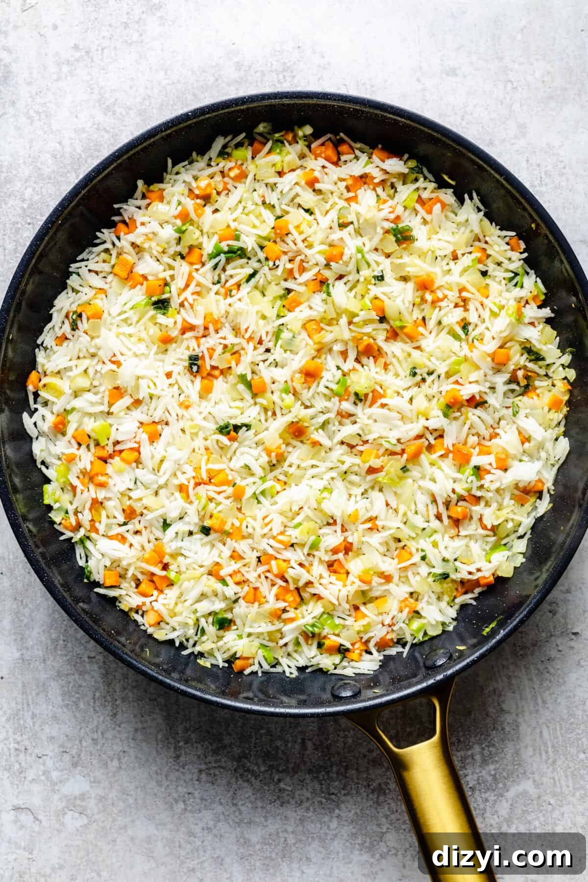 Rice added to the veggies in a black skillet with a gold handle for Simple Chicken Fried Rice.