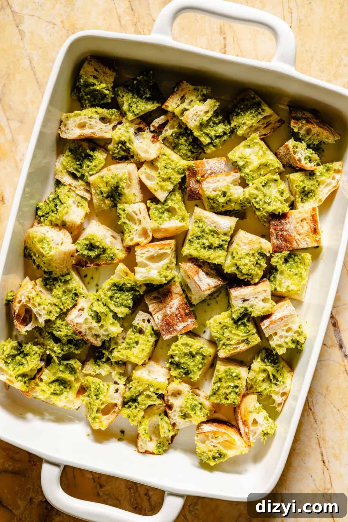 Ciabatta bread cut and covered in pesto in baking dish.