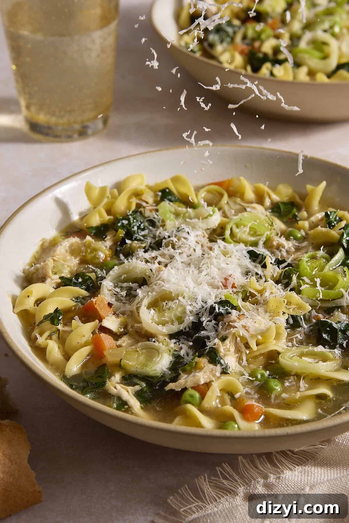 Classic Chicken and Leek Noodle Soup Recipe 3 Chicken and Leek Noodle Soup in bowl with parmesan being ladled on top.