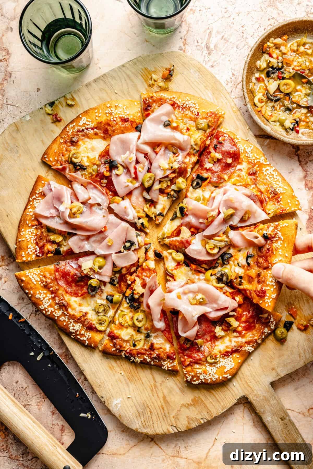 Grilled Muffaletta Pizza Recipe 6 Hand grabbing slice of Grilled Muffaletta Pizza off pizza peel.