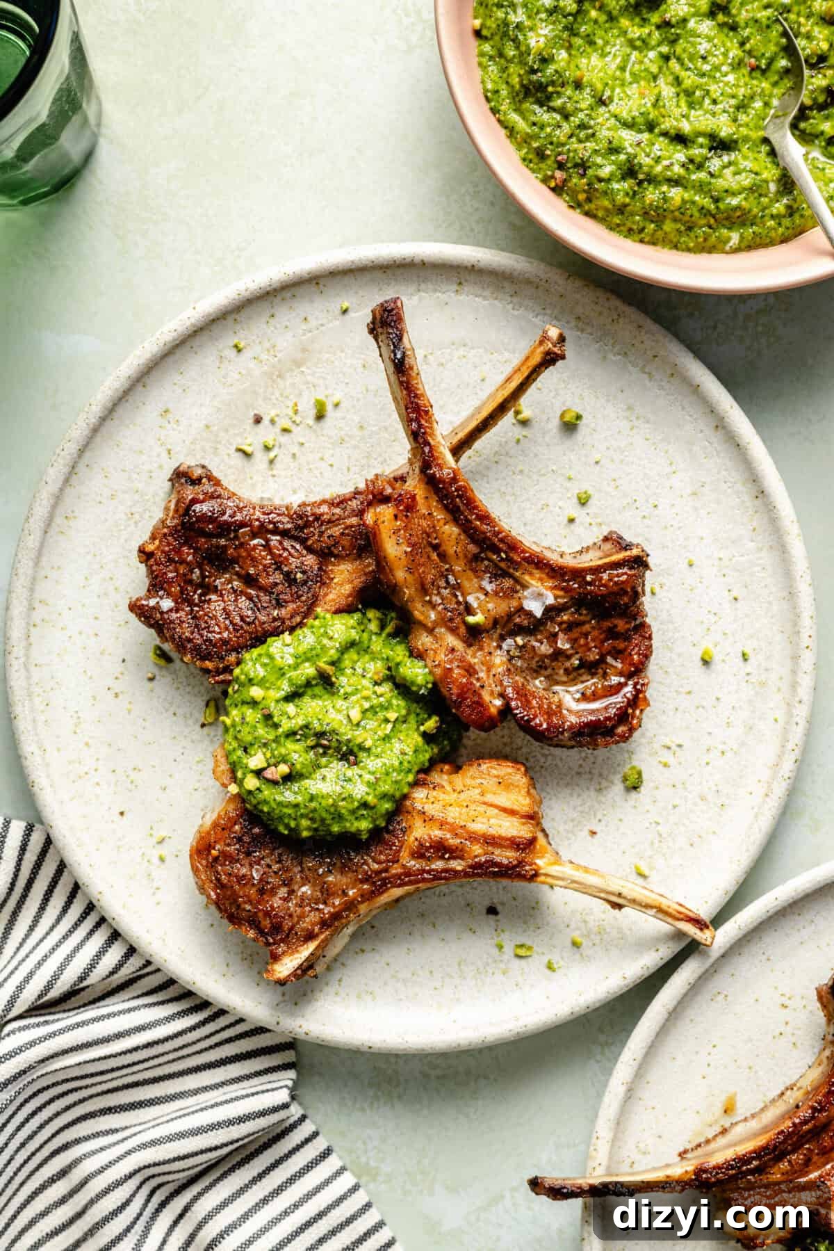 a white plate with three lamb chops topped with a dollop of arugula-pistachio pesto