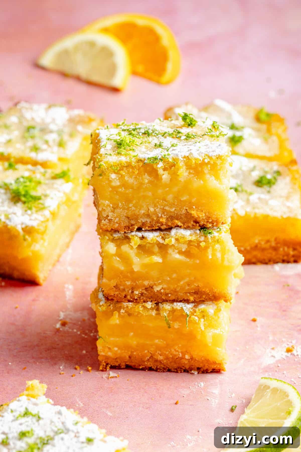 three citrus bars stacked on top of each other with citrus wedges scattered around on a pink background