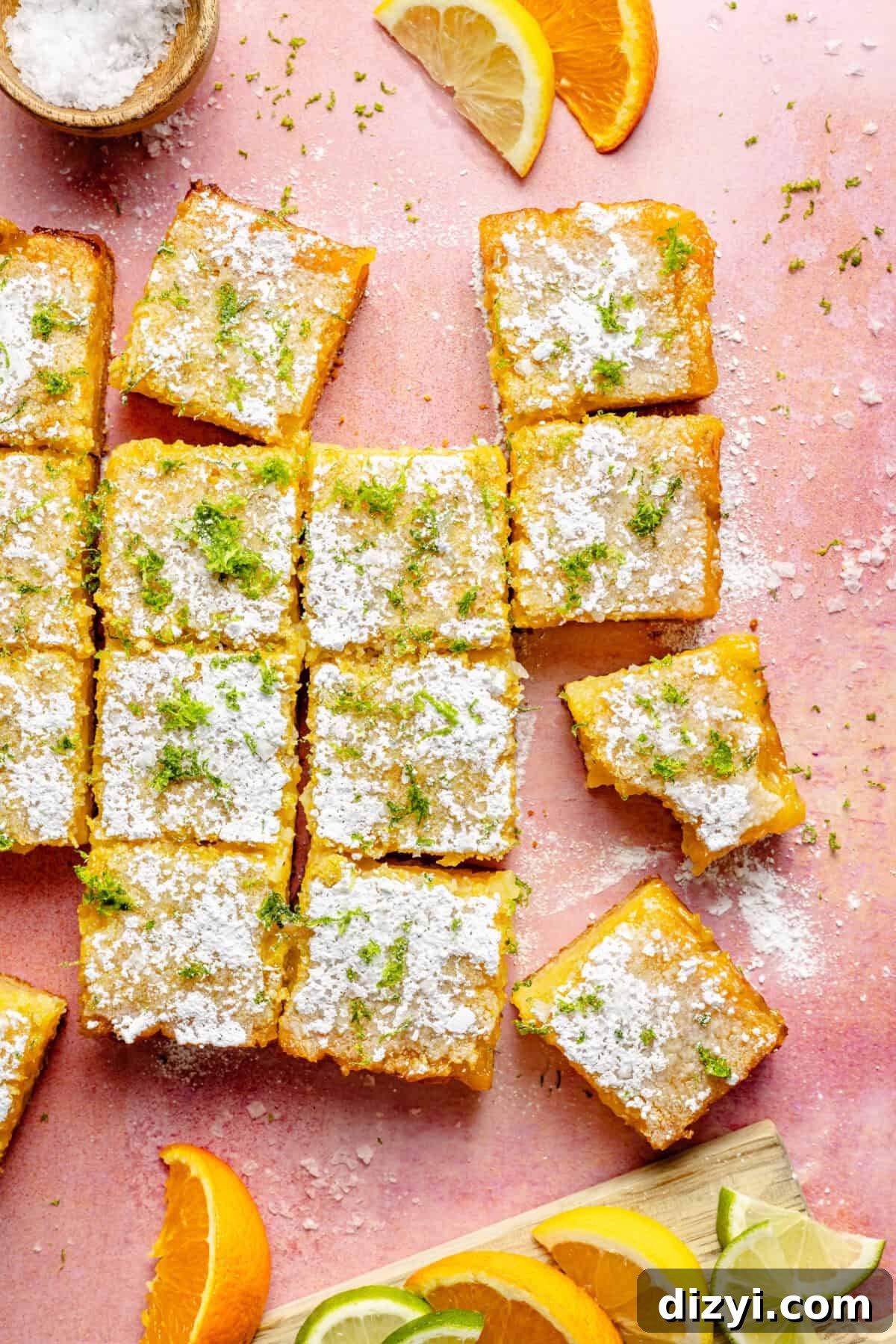 sliced citrus bars garnished with powdered sugar and lime zest on a pink background