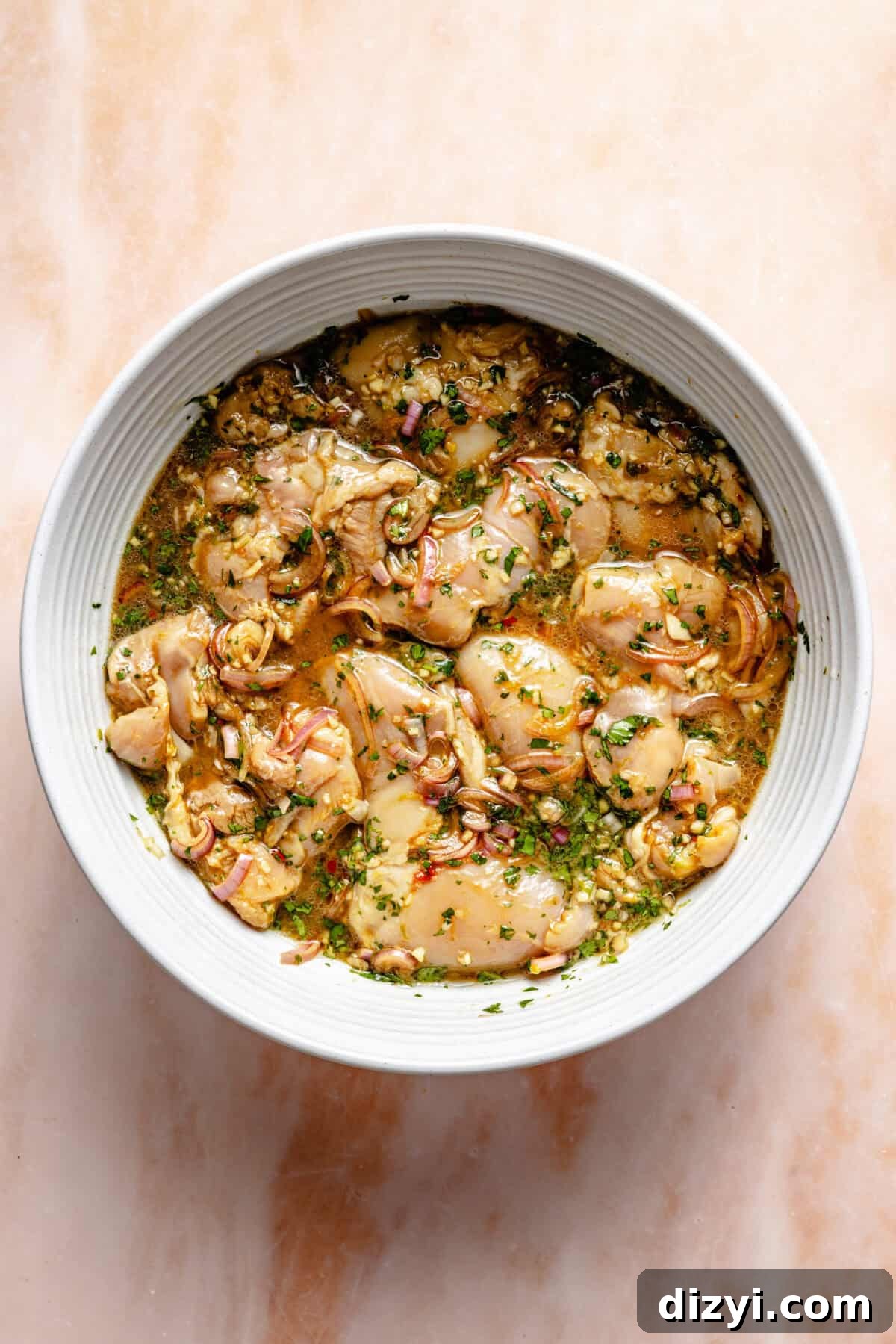 Vietnamese Chicken Noodle Bowls with Lime and Fresh Herbs 3 a white bowl with marinated chicken thighs on a light pink background