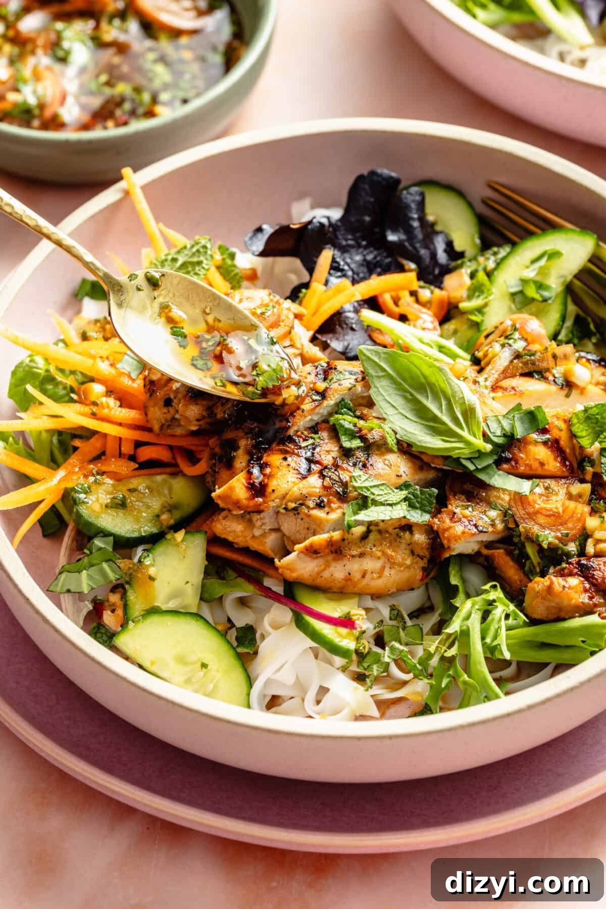 Vietnamese Chicken Noodle Bowls with Lime and Fresh Herbs 5 a close-up of a light pink bowl with rice noodles, chicken, vegetables, and Thai basil