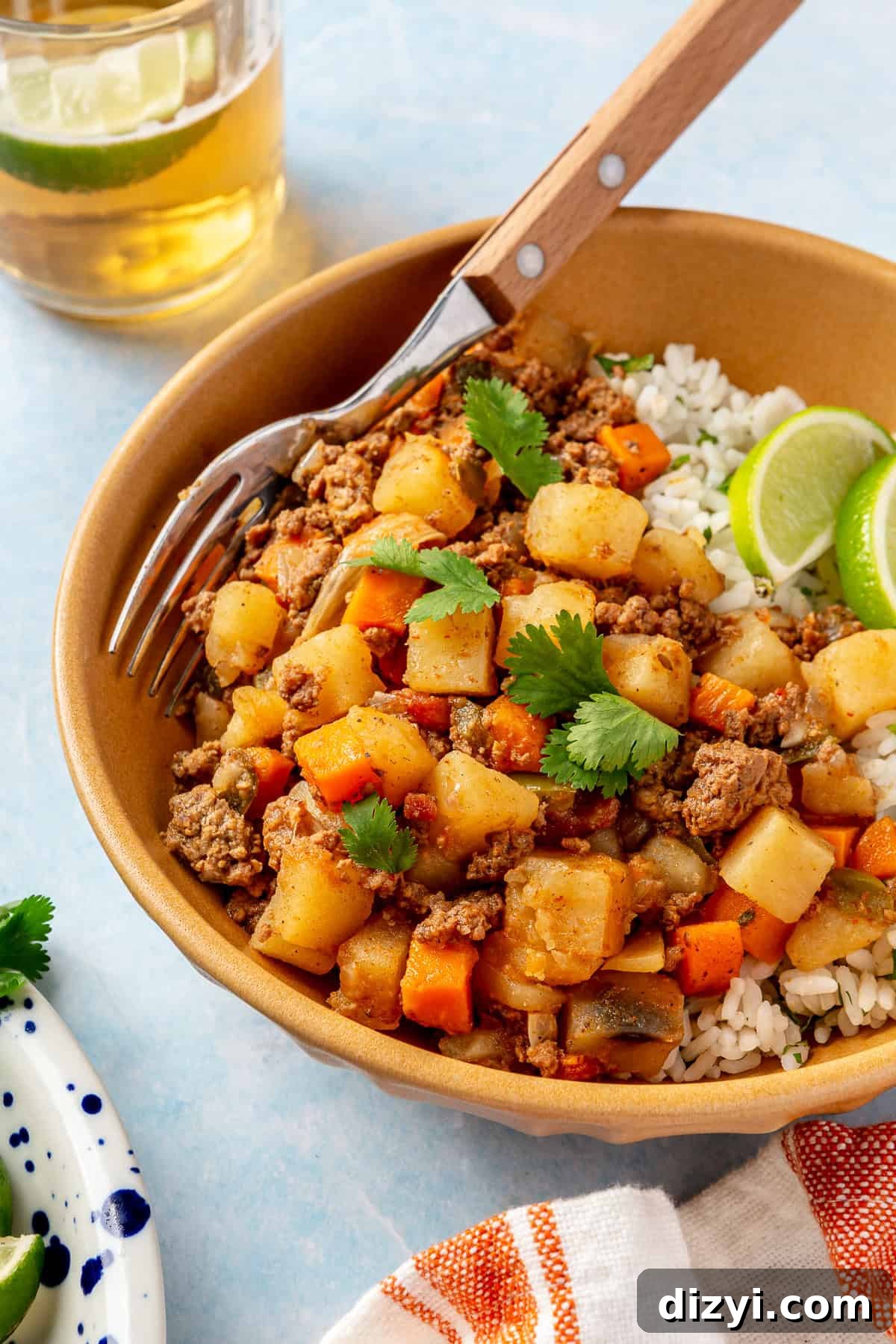 A close up shot of the finished Crockpot Mexican Picadillo in an orange bowl served with rice and garnished with lime and cilantro.