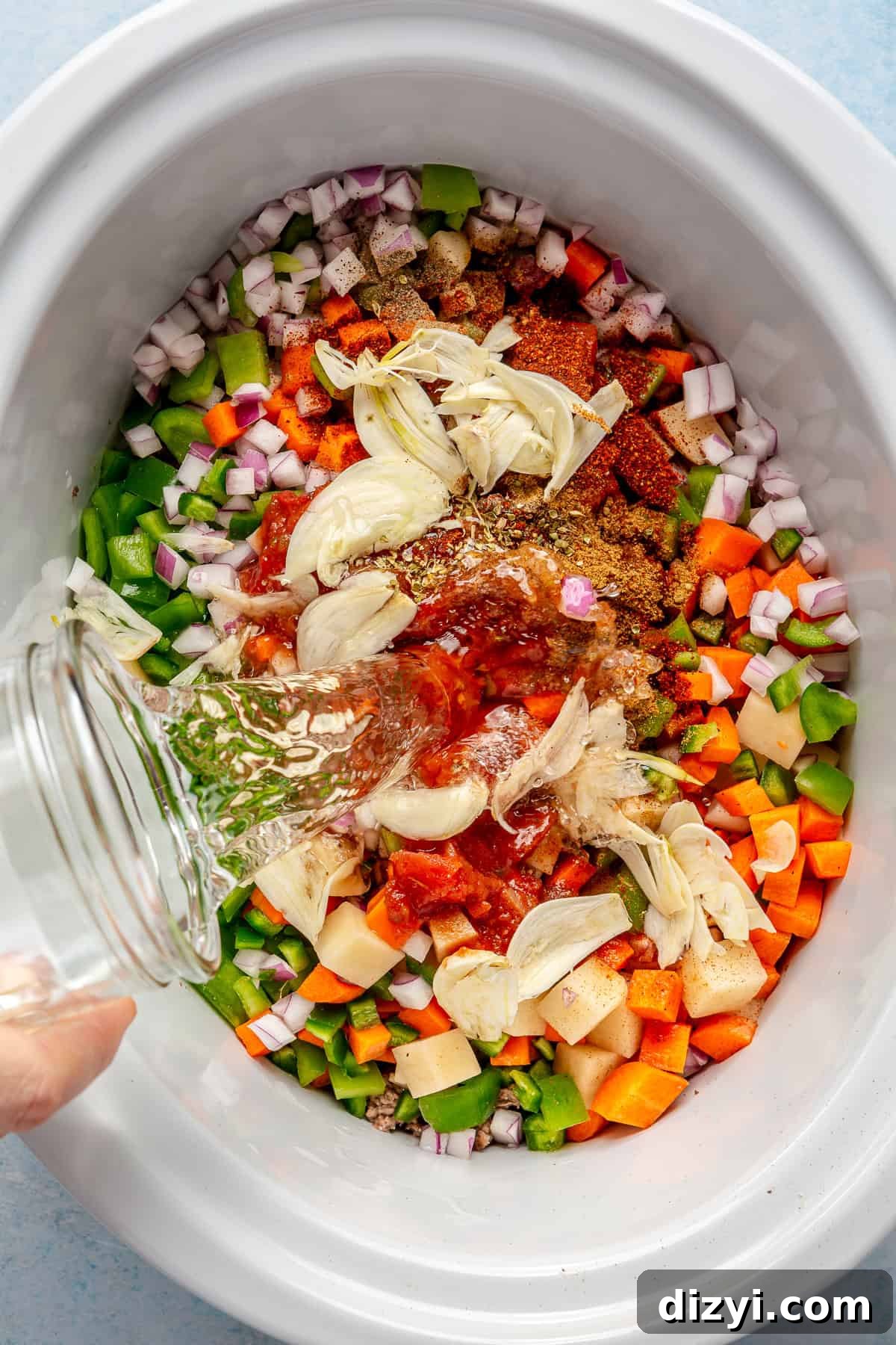 The ingredients for the Crockpot Mexican Picadillo added to a crockpot with a glass of water being poured into it.