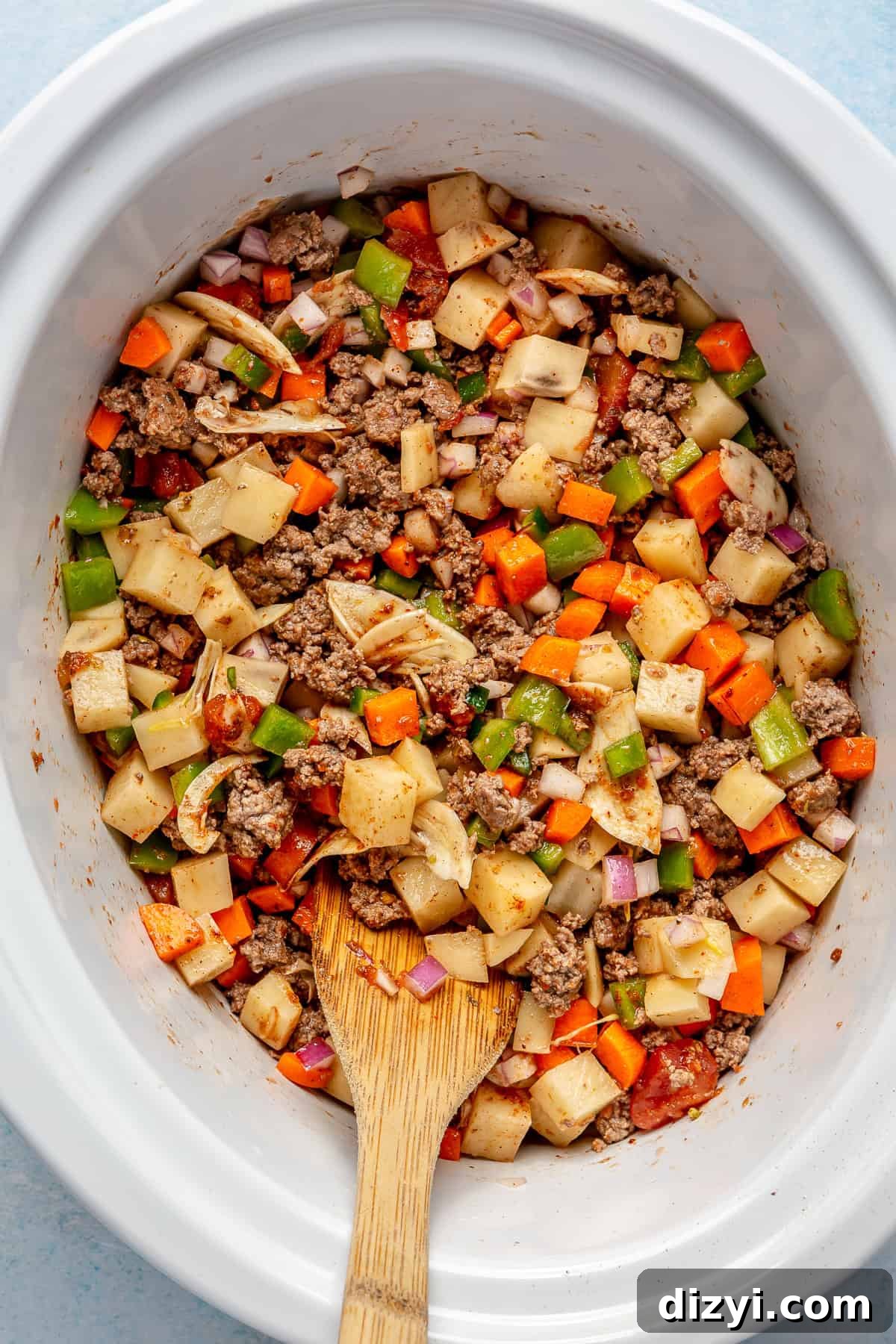The Crockpot Mexican Picadillo cooking in the slow cooker and being stirred with a wooden spoon.