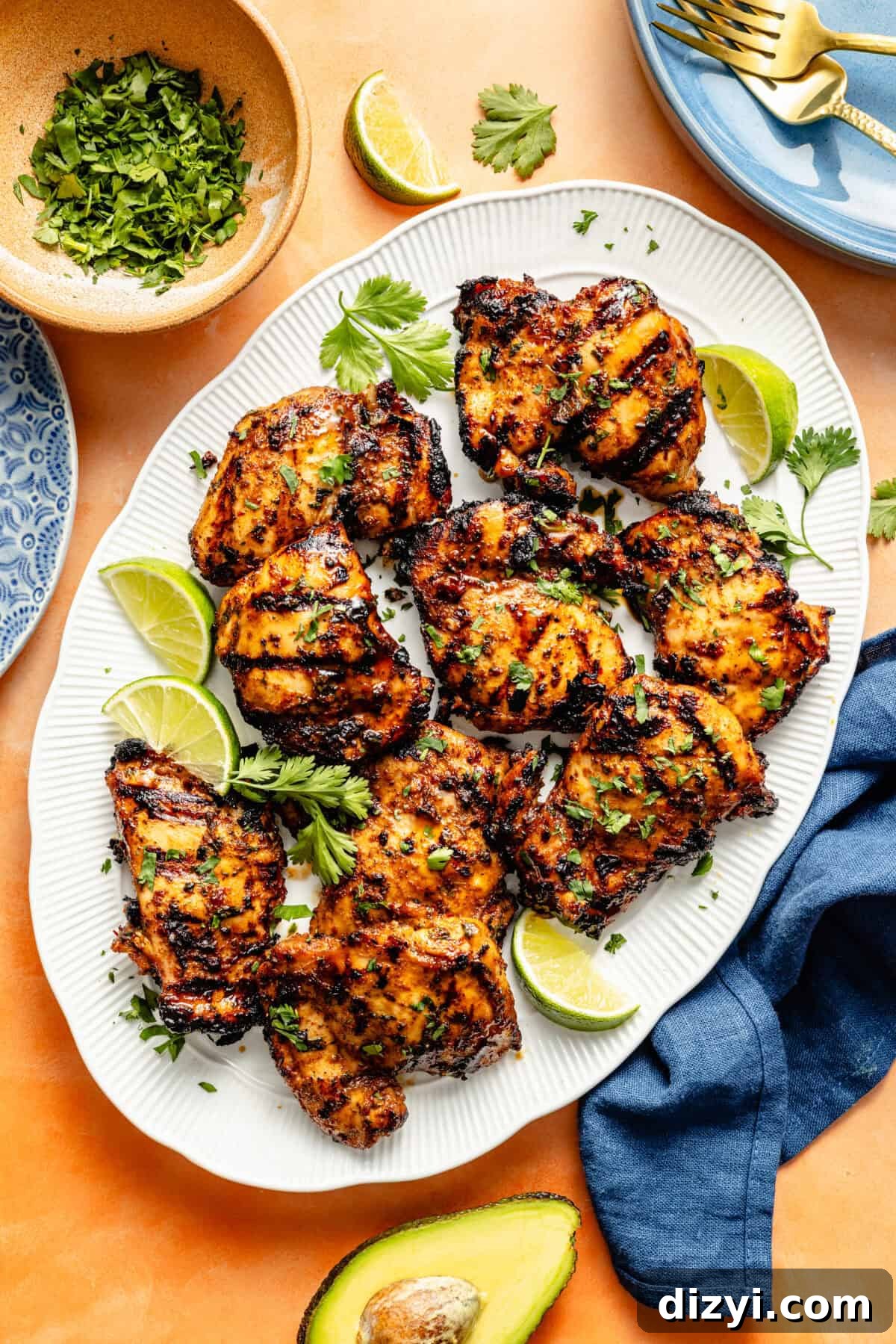 a white platter of grilled chicken with lime wedges on an orange background with a blue napkin