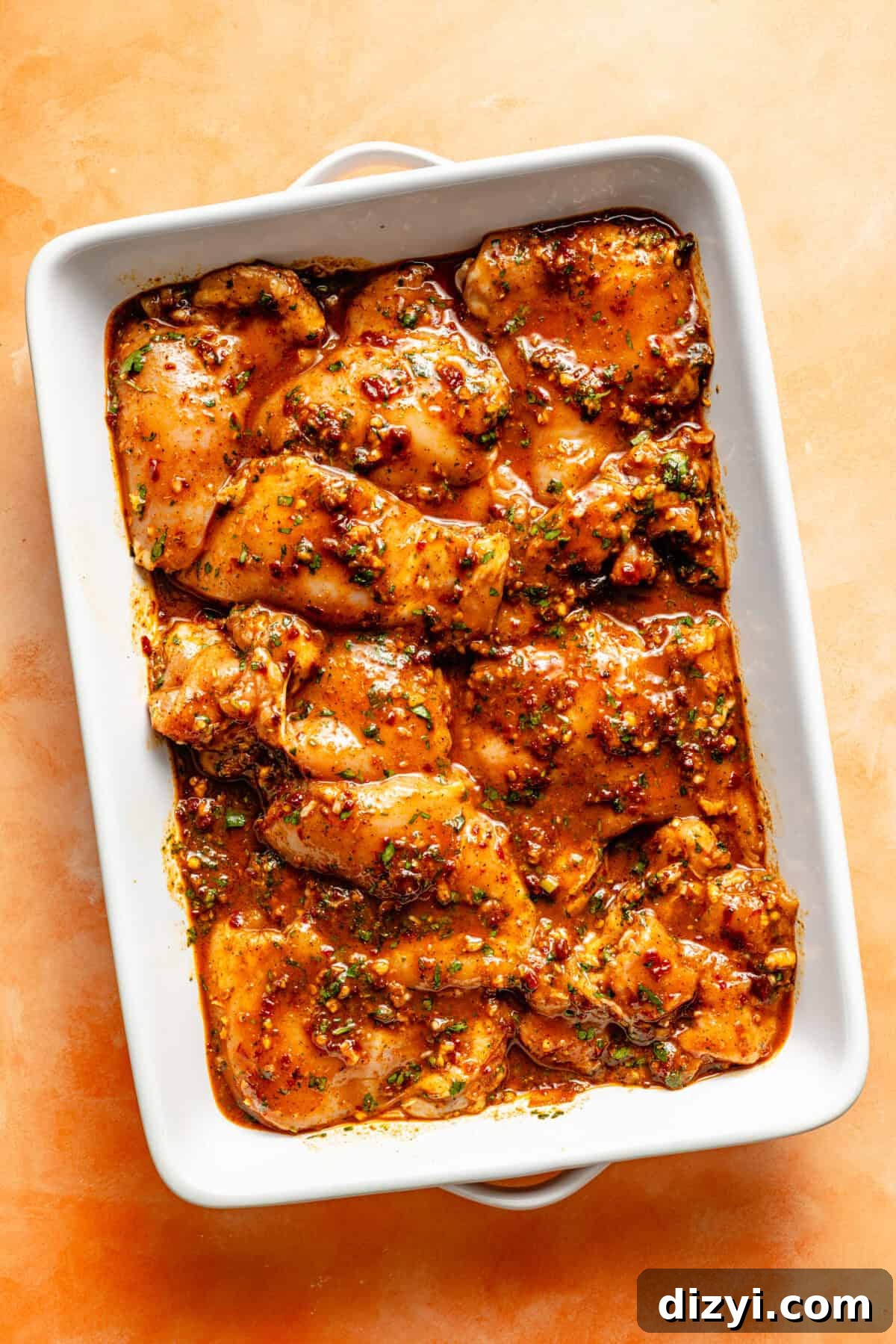 a white baking dish of marinated chicken on an orange background