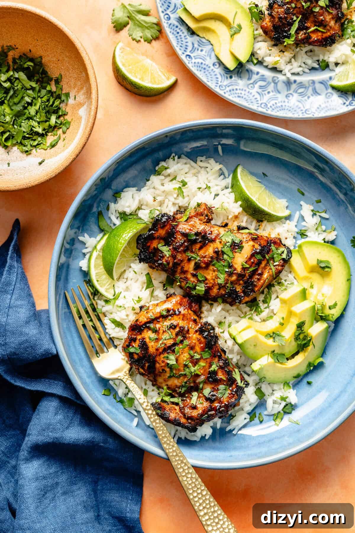 a blue bowl with rice with grilled chicken, avocado slices, and lime wedges on a light orange background
