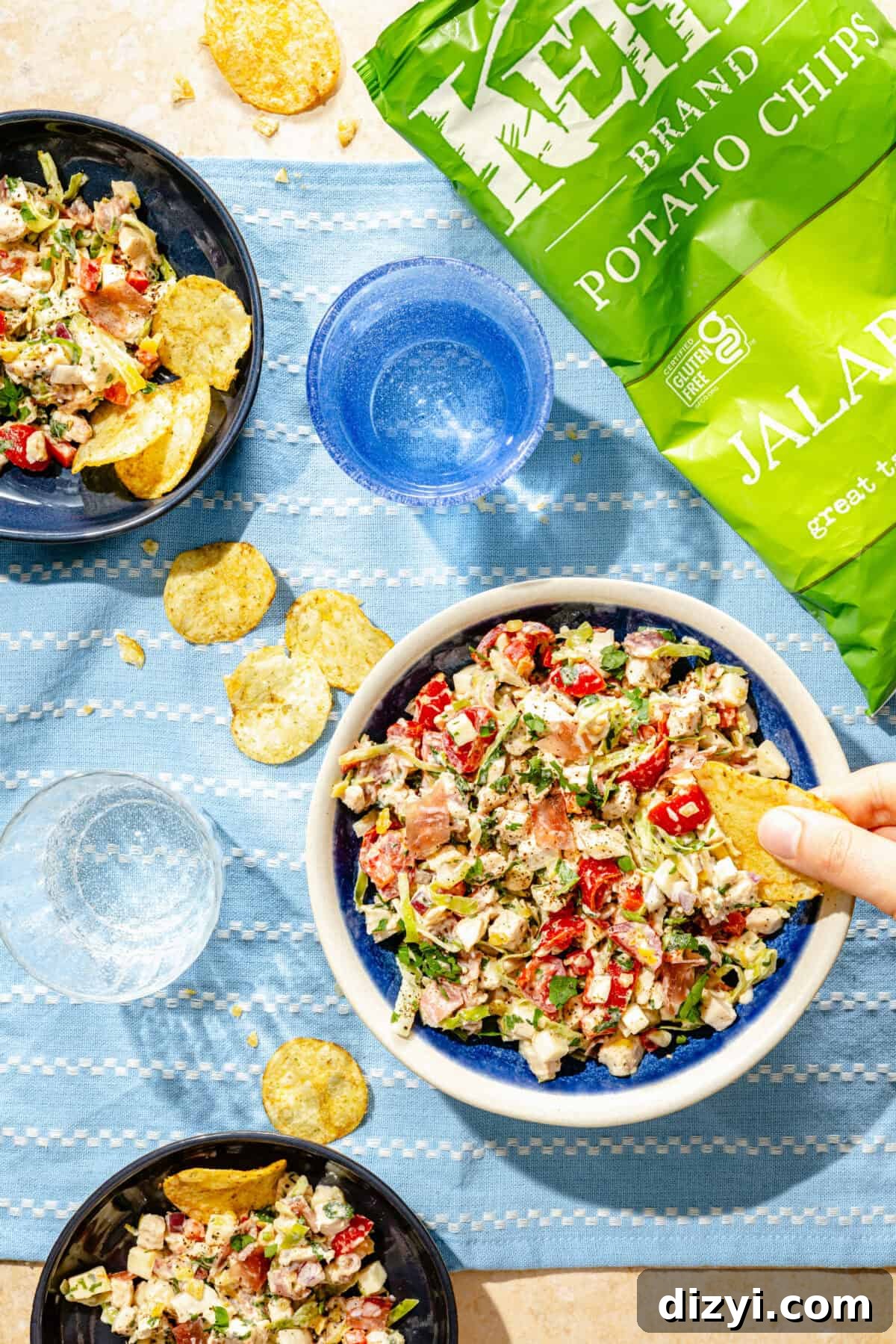 Deli-Style Chopped Chicken Salad Recipe 2 three bowls of chicken salad with vegetables on a blue background with a bag of jalapeño potato chips
