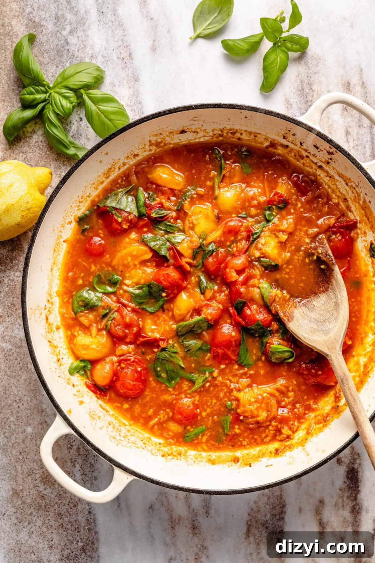 a deep enameled cast-iron skillet with burst tomato sauce and fresh basil