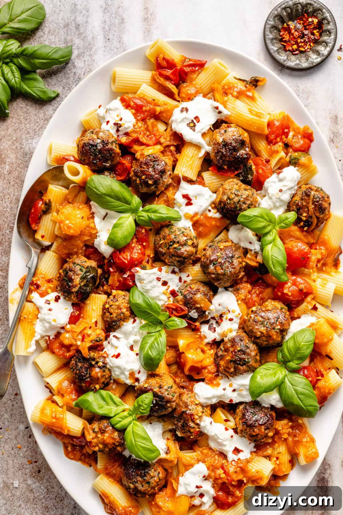 a white platter with cooked pasta, meatballs, burst tomatoes, fresh basil, and burrata cheese