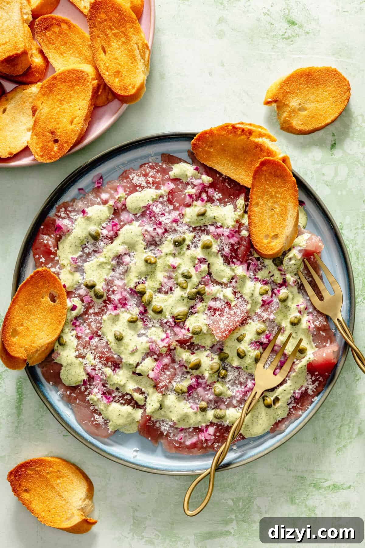 a light blue plate with pounded raw tuna, basil aioli, capers, and toasted crostini