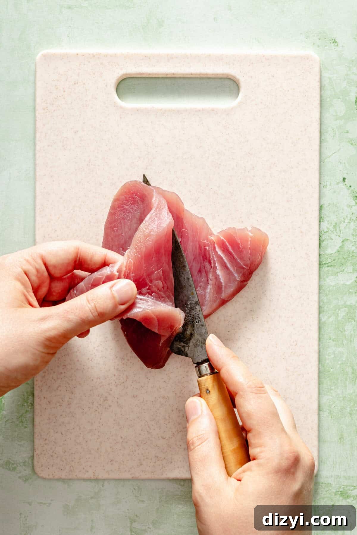 a cook slicing a piece of thick-cut of tuna on a white cutting board and light green background