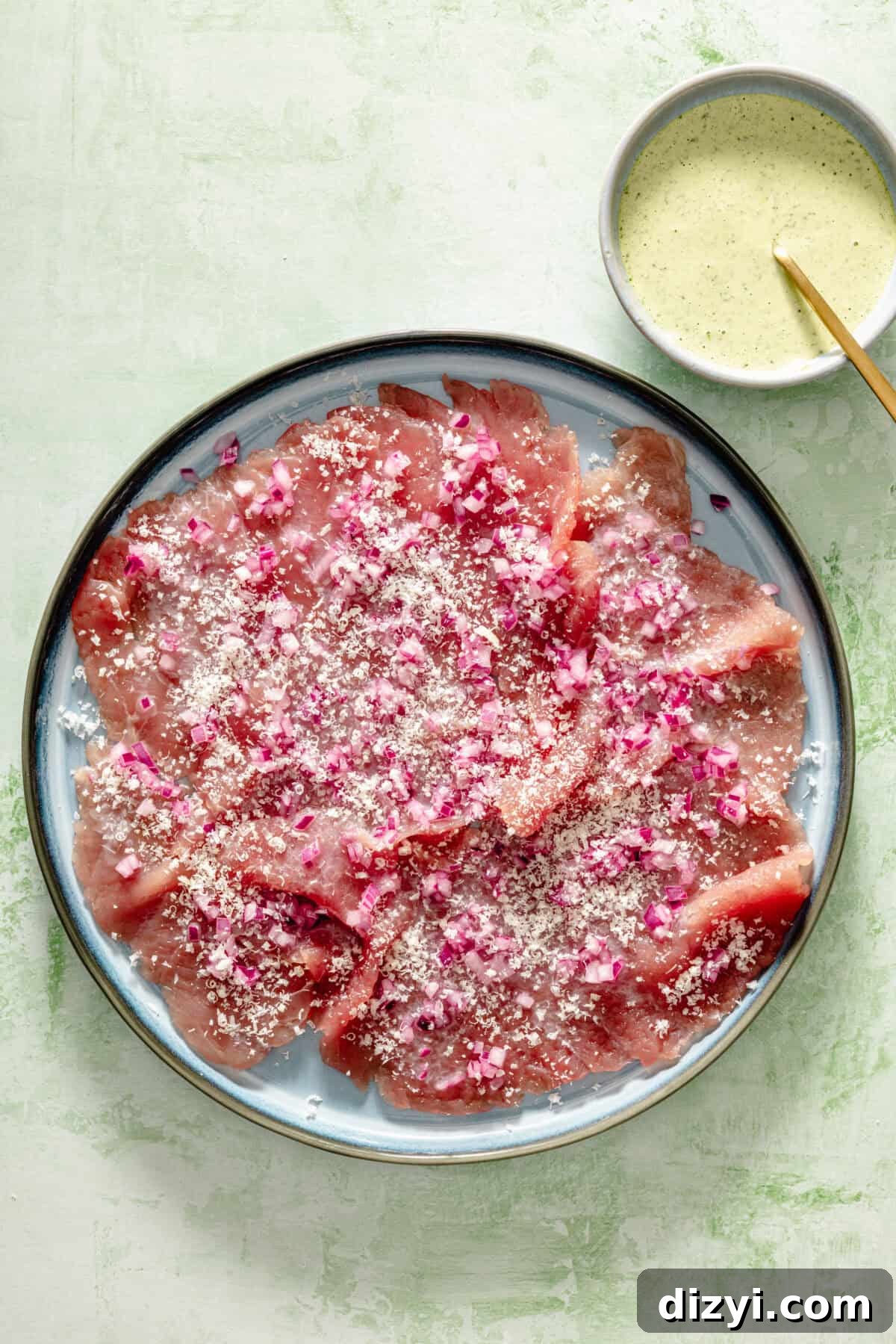 a plate of thinly sliced tuna topped with marinated red onions on a light blue plate and light green background