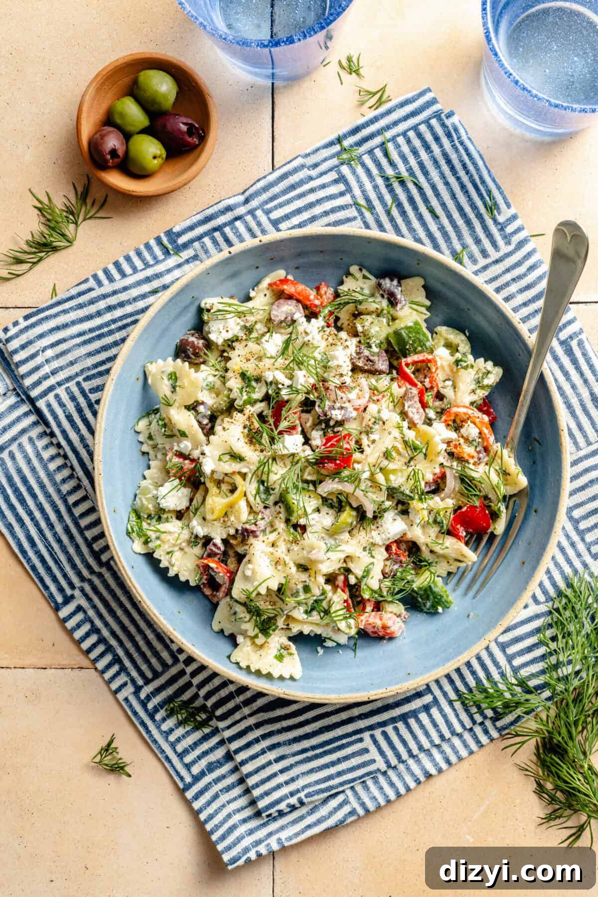 Classic Greek Pasta Salad with Feta and Kalamata Olives 2 a bowl of Greek pasta salad with fresh vegetables and herbs placed on a blue and white napkin