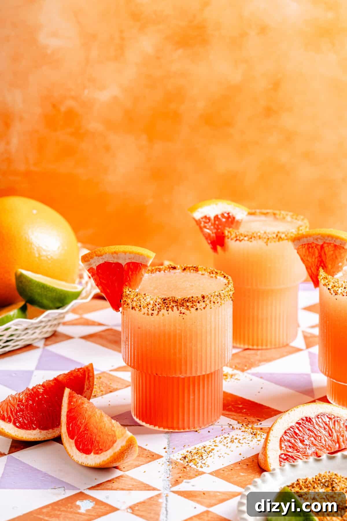 two glasses with frozen paloma cocktail, chile-lime rim, and grapefruit wedges on an orange background
